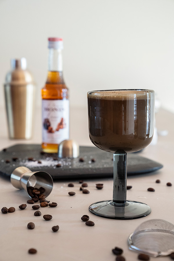 Espressomartini gepresenteerd in een Bubble glazen wijnglas, omgeven door koffiebonen en baraccessoires.